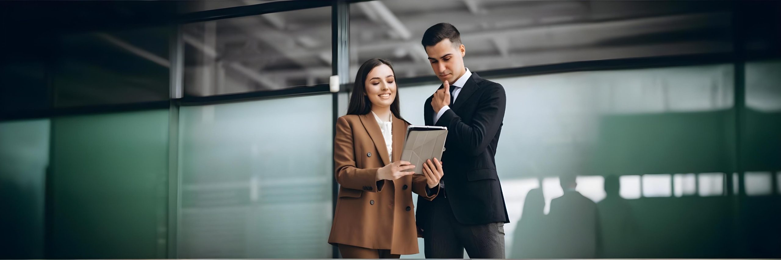 Dois profissionais analisando dados em tablet em ambiente corporativo.