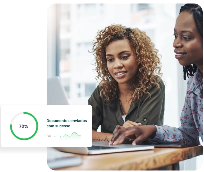 Duas profissionais analisando documentos no notebook com indicador visual de documentos enviados com sucesso.