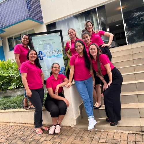 Equipe da contabilidade Mais Contábil reunida em frente ao escritório, usando camisetas rosas personalizadas.