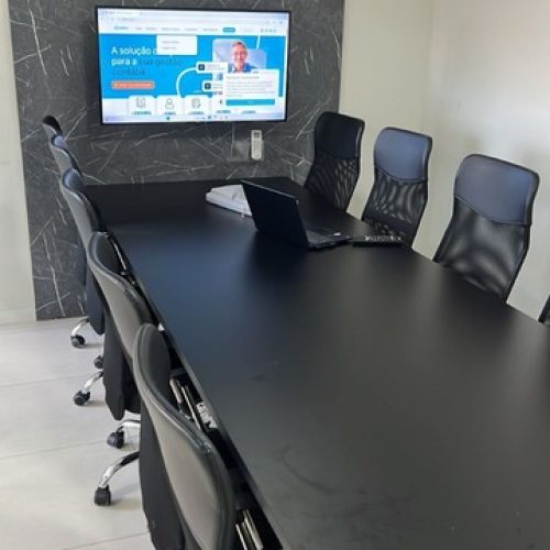 Sala de reunião moderna com mesa ampla, cadeiras ergonômicas e tela para apresentações